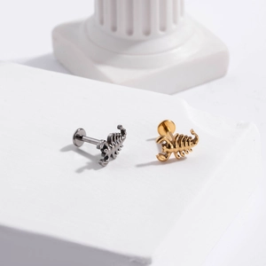 Detail view of scorpion-shaped G23 titanium labret studs in silver and gold finishes