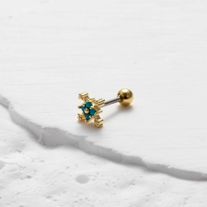 Macro-opname van gouden piercing met turkoois stenen op witte steentextuur
