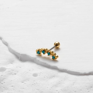 Macro-opname van goudkleurige kraakbeenpiercing met vier turquoise stenen op steen