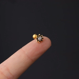Detail view of a 16G gold starburst cartilage stud with zircon on a fingertip
