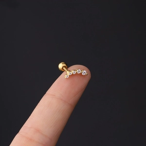 Detailed view of gold curved zircon cartilage piercing held on fingertip for scale
