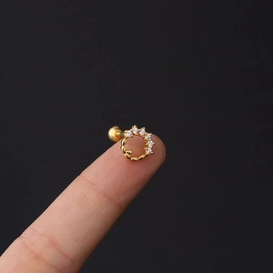 Detailed view of a 16G gold cartilage stud with five white zircons on a fingertip