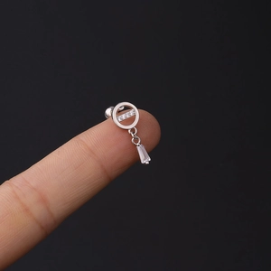 Detailed macro view of silver tragus piercing with zircon circle and rectangular crystal drop