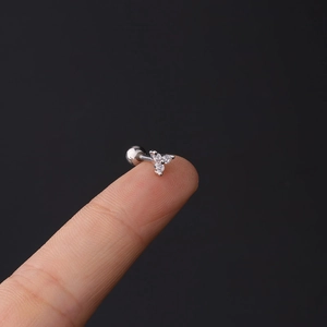Detailed view of tiny three-stone clover cartilage stud on a finger for size comparison