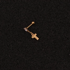 Détail d'un piercing en acier doré avec pendentif en croix étoilée et pierre de zircon cubique