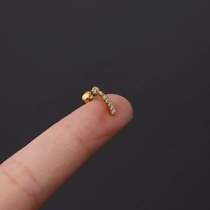 Macro shot of tiny gold-tone curved cartilage earring with crystals on a fingertip