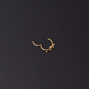 Detail eines goldenen Edelstahl-Clicker-Hoops mit Blattgravuren auf schwarzem Hintergrund