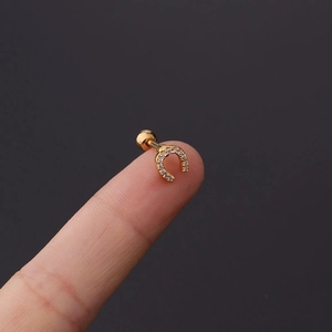 Macro shot of gold-plated horseshoe ear stud with zircon inlay held on a fingertip