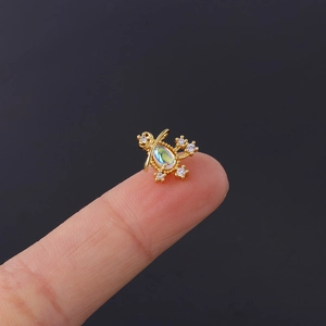 Macro view of gold opal earring with crystal accents on a fingertip for size comparison