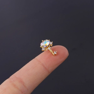 Macro shot of a tiny gold key earring with AB iridescent stone held on a finger tip