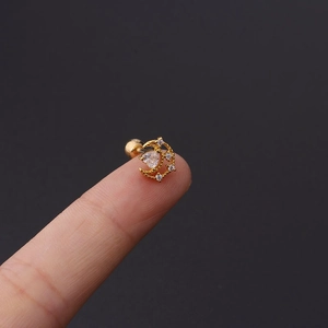 Detailed view of a gold moon cartilage earring with cubic zirconia held by hand