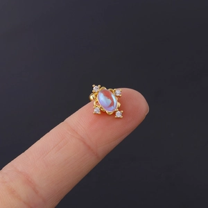 Macro shot of 20G gold moonstone cartilage stud with white zircon accents on fingertip