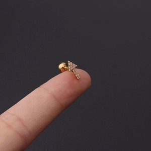 Close-up of a small gold arrow cartilage stud earring with cubic zirconia on a fingertip