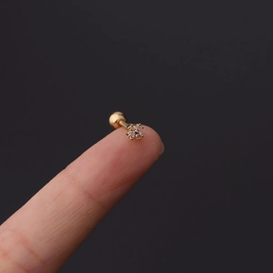 Macro shot of a tiny gold flower cartilage stud with clear zircons on a fingertip
