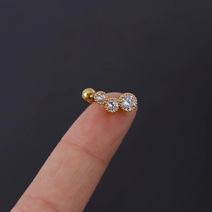 Macro detail of gold curved cartilage stud featuring three graduated clear zircons and screw ball
