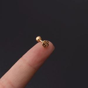 Detailed close-up of golden rose cartilage earring with screw ball back on a fingertip