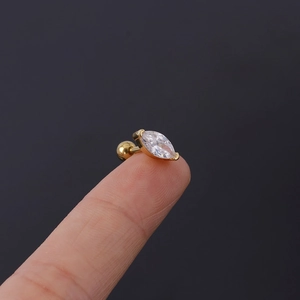 Macro shot of gold-plated piercing stud with marquise-cut crystal held on fingertip