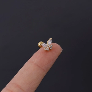 Macro detail of gold butterfly cartilage stud with white zirconia stones on fingertip