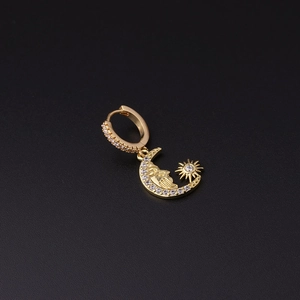 Detailed close-up of a gold celestial hoop earring with moon and sun charms on black background