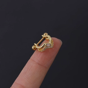 Vue macro d'un clou d'oreille en V doré avec zircons posé sur un doigt