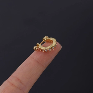 Détail macro d'un petit piercing d'oreille doré serti de zircons posé sur le bout du doigt