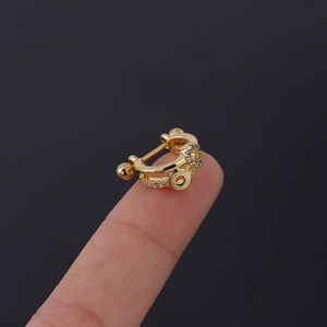 Gros plan d'un piercing d'oreille doré avec zircons brillants tenu par les doigts