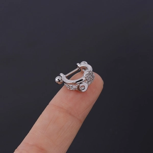 Vue macro d'un piercing d'oreille argenté serti de zircons tenu entre les doigts de main