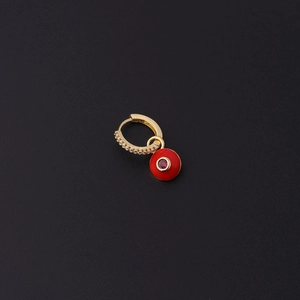 Détail macro d'une boucle d'oreille dorée avec zircons et pendentif œil en émail rouge