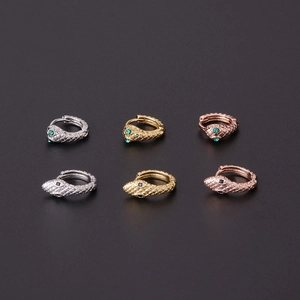 Detailed macro view of snake-shaped earrings with green gemstone eyes in various metal colors