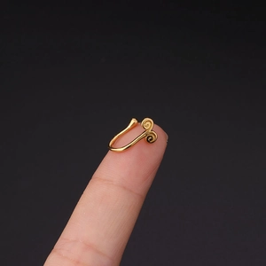 Detailopname van een gouden U-vormige neusclip met dubbel spiraalpatroon op een vingertop