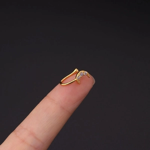 Macrodetail van een goudkleurige maanvormige clip-on neusring met drie heldere zirkonia's