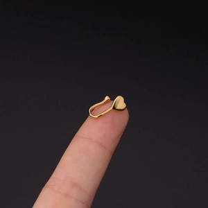 Macro-opname van een goudkleurige hartvormige nep neuspiercing clip op een vingertop