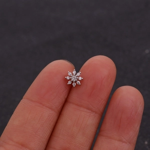 Macro-opname van een kleine zilveren sneeuwvlok oorknopje vastgehouden tegen een vingertop
