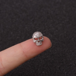 Vista macro de un pequeño colgante de calavera plateado con cristales sobre la punta del dedo