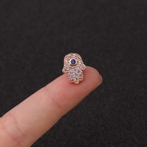 Macro de pendiente de mano de Hamsa en oro rosa con ojo azul sobre la punta del dedo