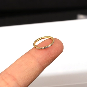 Macro detail of a golden stainless steel hinged hoop ring with side-set cubic zirconia