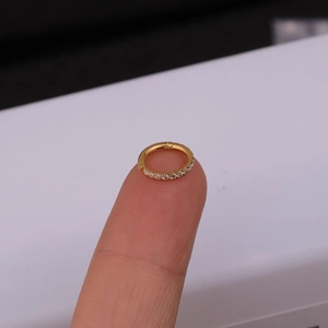Macro shot of a tiny gold stainless steel hinged ring with side-set cubic zirconia on a fingertip