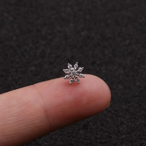 Macro shot of tiny snowflake cubic zirconia stud earring held on a fingertip for scale