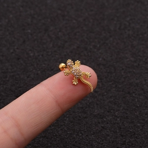 Detailed macro shot of a rose gold gecko stud earring with zircon inlay on a finger