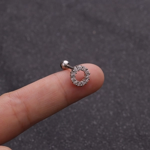 Primo piano di un orecchino barbell in argento con zirconi scintillanti su un dito