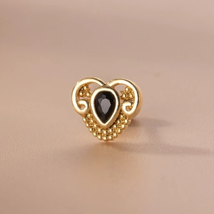 Dettaglio macro di un orecchino a cuore vintage con zircone nero e filigrana dorata
