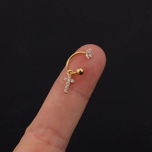Dettaglio di un piercing a croce dorato con pendente in zircone tra le dita