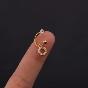 Macro di un orecchino a C dorato con pendente in zircone tenuto sulla punta del dito