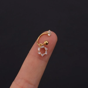 Dettaglio macro di un piercing dorato con pendente in zircone esagonale sulle dita