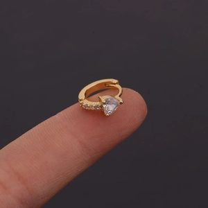 Gros plan de mini créoles en cœur et zircon doré portées sur le bout d'un doigt