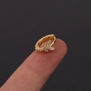 Gros plan d'une boucle d'oreille papillon dorée avec zircons posée sur un doigt