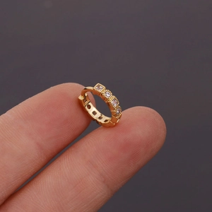 Gros plan sur une petite boucle d'oreille dorée sertie de quatre zircons carrés blancs