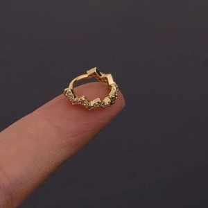 Détail d'une boucle d'oreille géométrique dorée avec zircons sur le bout du doigt