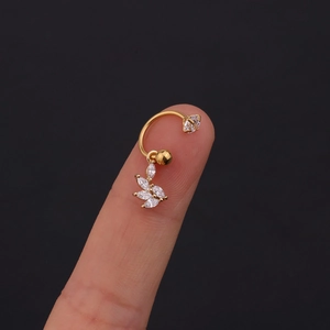 Dettaglio macro di un piercing dorato con fiore di zirconi tenuto tra le dita