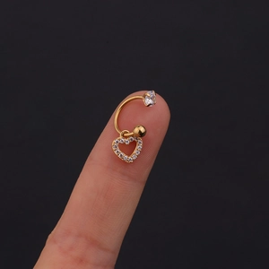 Dettaglio di un piercing a cuore dorato con zirconi bianchi tenuto tra le dita